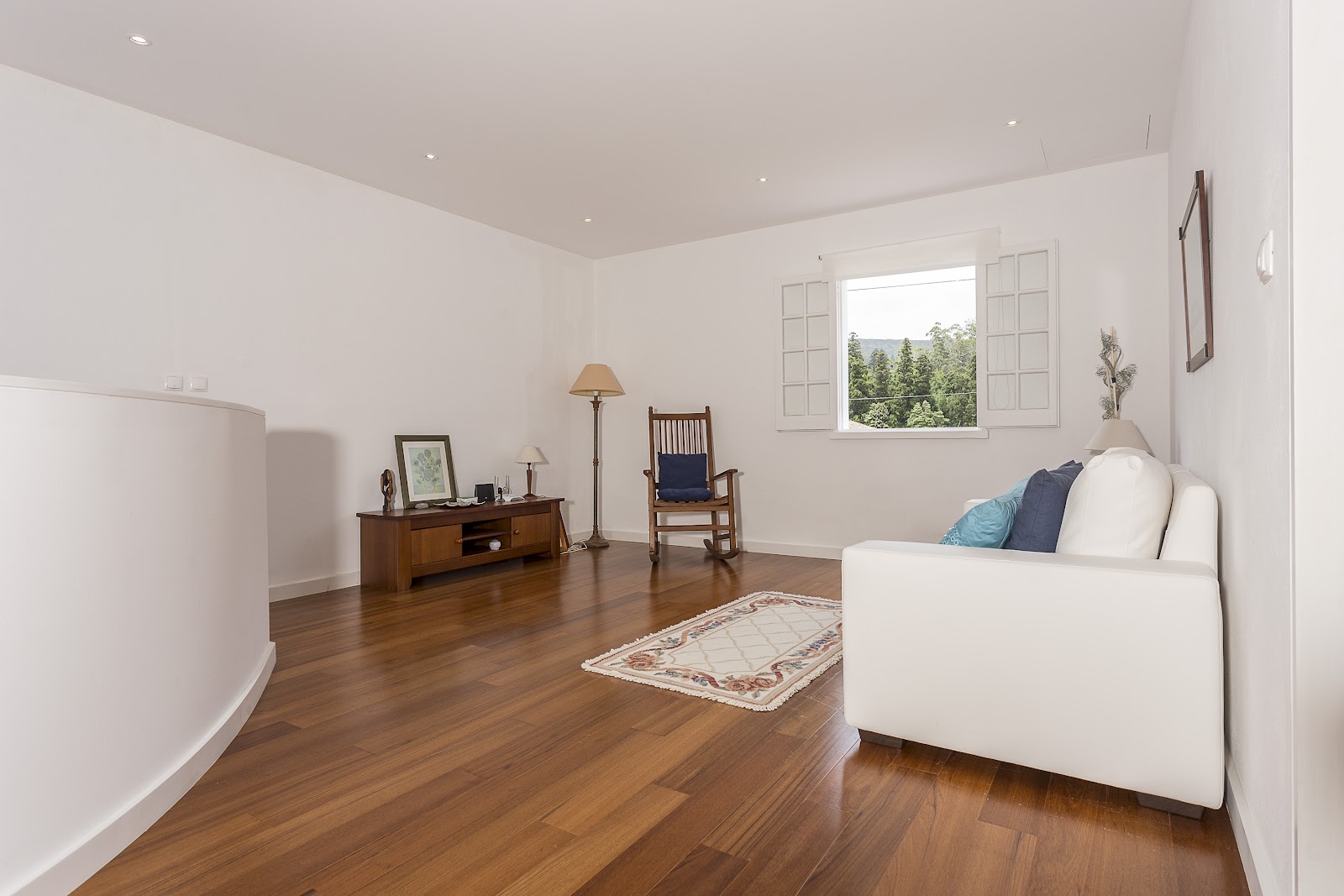 Upstairs lounge with white sofa, rocking chair, media unit, and window view